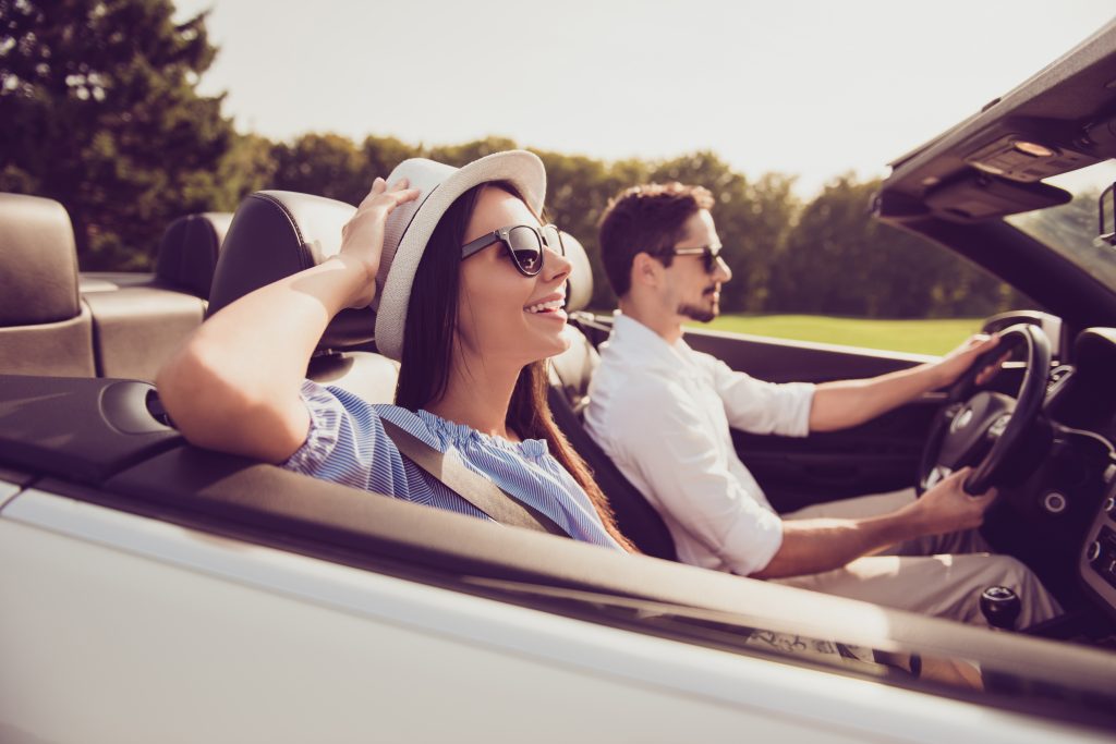 A woman and a man enjoying a drive in a convertible car on a sunny day.