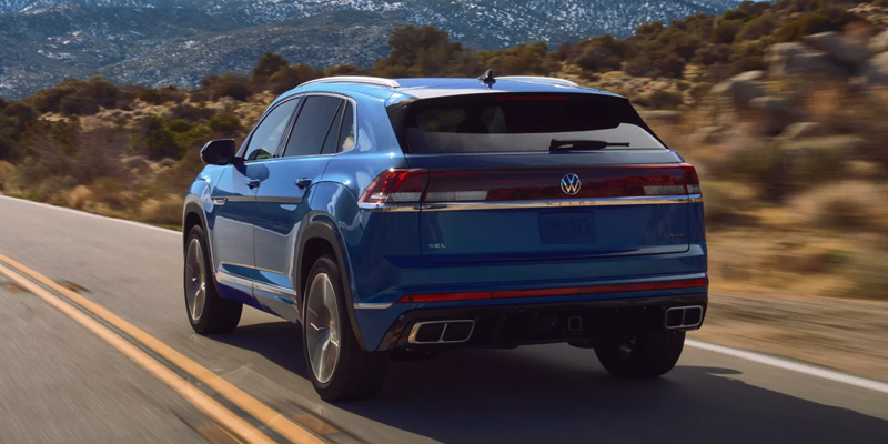 A blue Volkswagen SUV driving on a scenic road with mountains in the background