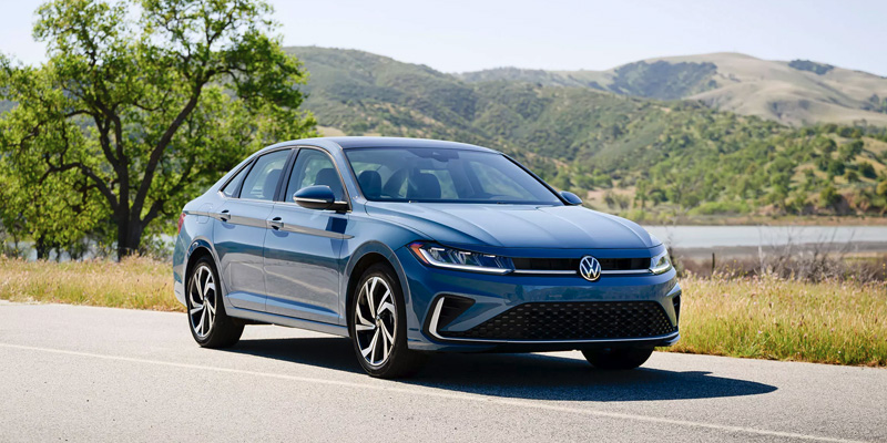 Blue Volkswagen Jetta sedan parked near a scenic landscape.
